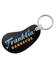Black bean shaped vinyl keychain with blue and orange Franklin Barbecue logo. A silver metal key ring on the right side.