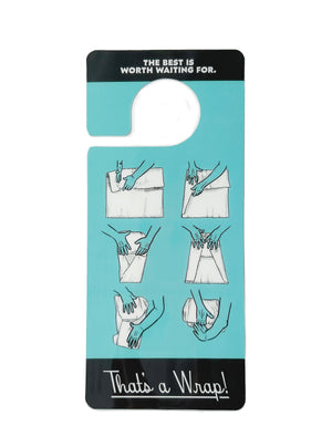 Back of turquoise blue door hanger.  On the top in white text surrounded by black it says, "The best is worth waiting for." Below that is six images in white and turquoise showing two hands folding a brisket in butcher paper. On the very bottom in white cursive text surrounded by black it says, "That's a wrap!"