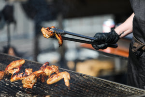 Image showing chef in black gloves flipping a chicken wing over a grill