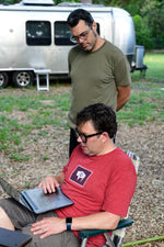 Aaron Franklin standing, glancing at a laptop with another man who is sitting down. Both look deep in thought. 