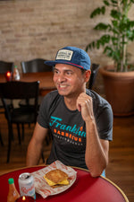 Man sits and enjoys a meal while wearing the navy blue hat.