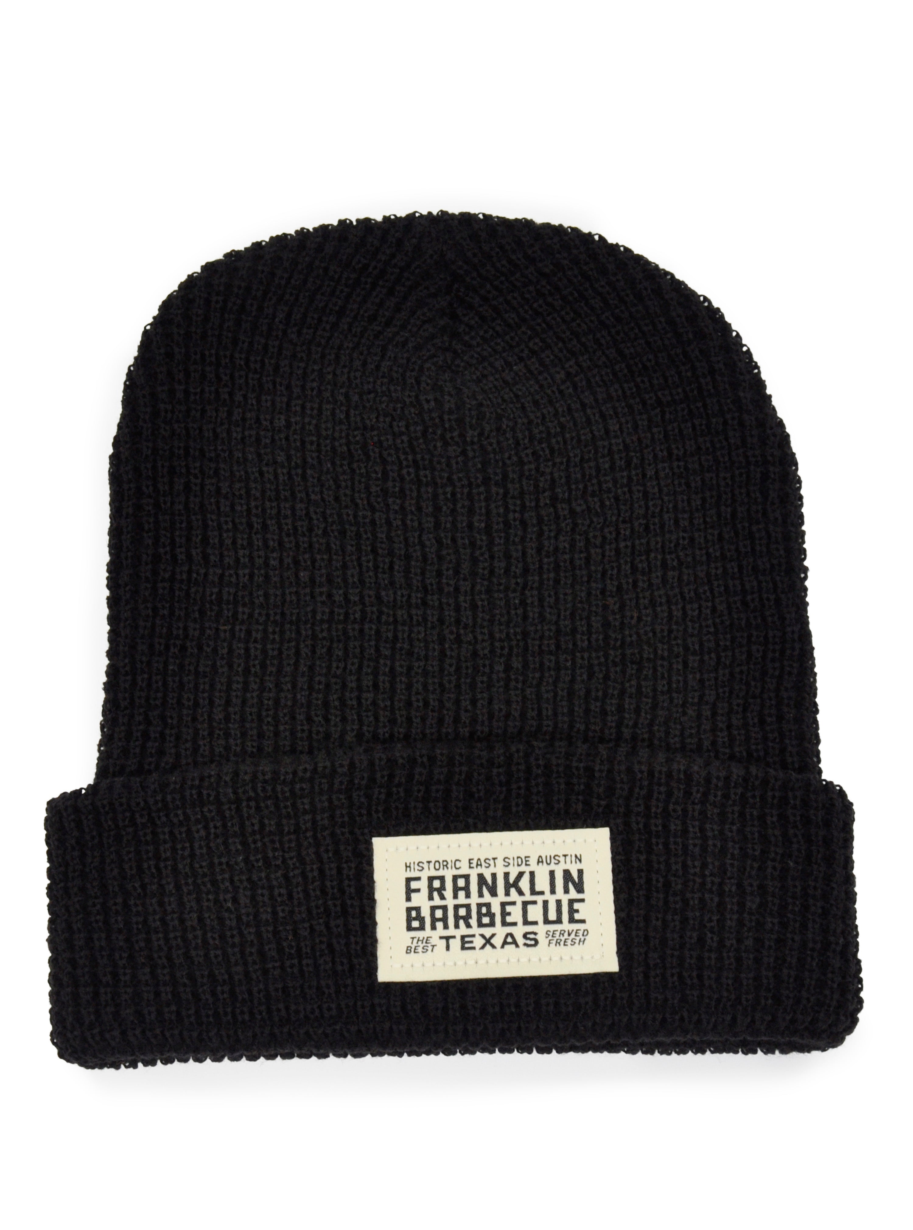 A black knit hat. The bottom is cuffed to reveal a small white sown on patch that says: "Historic East Side Austin. Franklin Barbecue. The Best. Texas. Served Fresh"