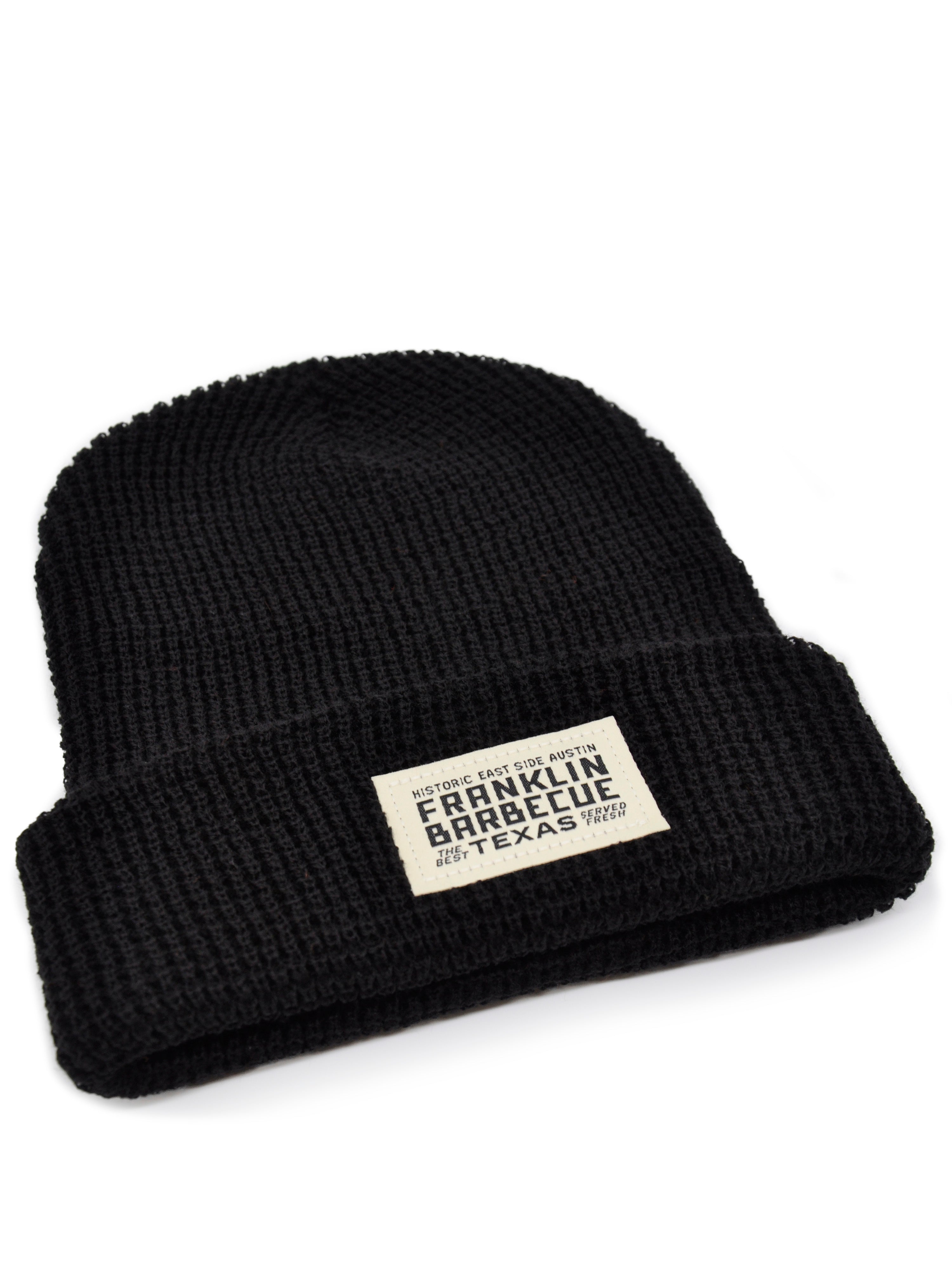 A black knit hat. The bottom is cuffed to reveal a small white sown on patch that says: "Historic East Side Austin. Franklin Barbecue. The Best. Texas. Served Fresh"