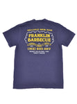 Back of navy blue t-shirt that reads in yellow and white letters: "900 E. 11th St. Austin, TX. Franklin Barbecue. It's served fresh daily until gone. 512-653-1187. Brisket, Pulled pork, Ribs, Turkey, Sausage". Beneath the words is an image of a cloud of smoke over three sausages.