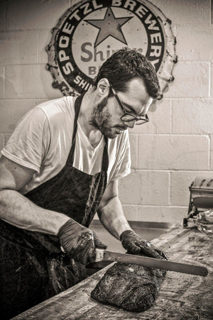 Black and white photo of Aaron Franklin using Franklin Dexter-Russell Scalloped knife with serrated stainless steel blade and white plastic handle to cut brisket