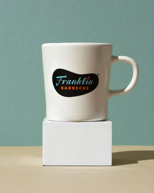 White mug with Franklin Logo in blue and orange lettering. Mug is on pedestal