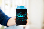 A person holding A can in a Black coldie holdie with Franklin Barbecue bean logo outlined in blue with Austin Texas below it also in blue. 