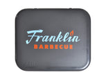 Close up on lid of Gray Franklin Yeti Roadie cooler with blue and orange Franklin Barbecue logo and embossed YETI logo on bottom left corner