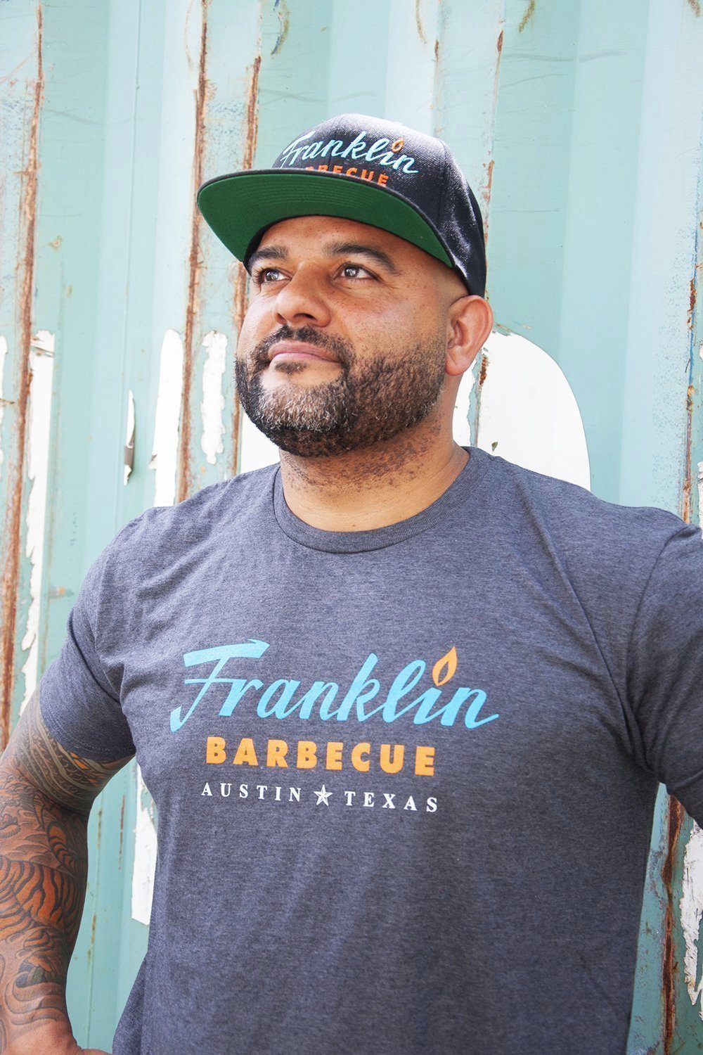 Person modeling Grey t-shirt with Franklin Barbecue text logo in blue and orange. Below that is Austin Texas in white.