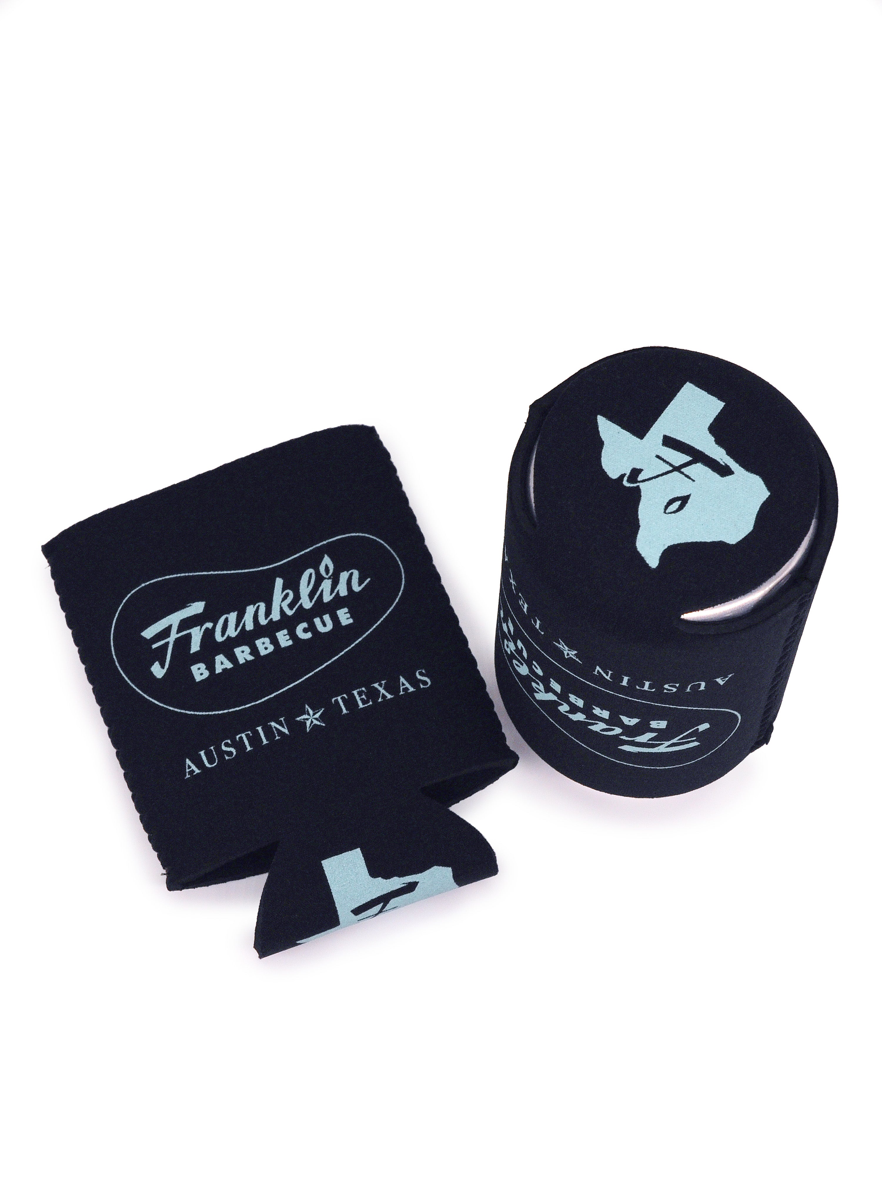 Two Black coldie holdie with Franklin Barbecue bean logo outlined in blue with Austin Texas below it also in blue; one is laid flat the other is shown with can inside displaying the bottom design of the shape of Texas in blue and Franklin 'F' in the middle