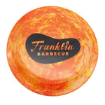 Orange-swirl Franklin Frisbee with screen printed logo of Franklin Barbecue bean in black